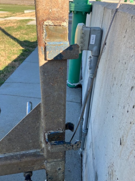 Steel brackets welded to a gate frame against a concrete wall, welded in place on site.