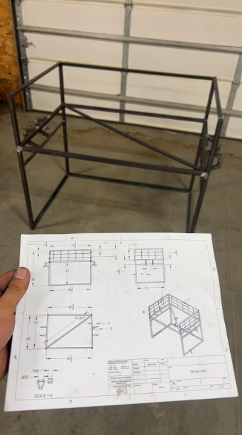 Welded rack frame held up against its dimensioned shop drawing outside the shop door.