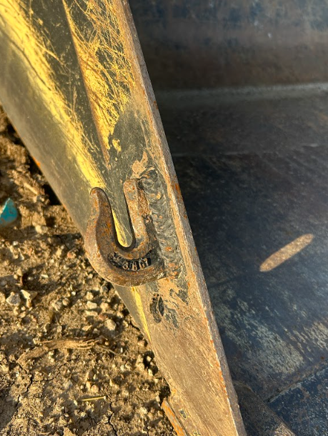 Rated lifting hook welded onto the edge of a loader bucket.