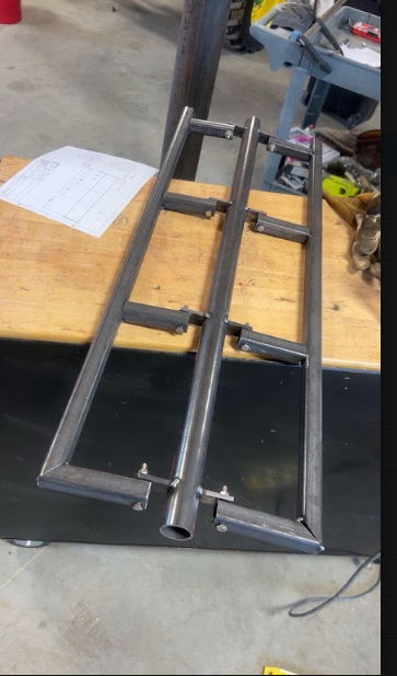 Two welded tube assemblies laid out on the bench beside the drawings they were built from.